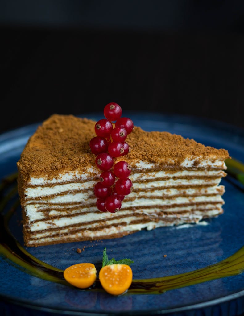 Close-up of a layered cake slice topped with red currants on a blue plate.