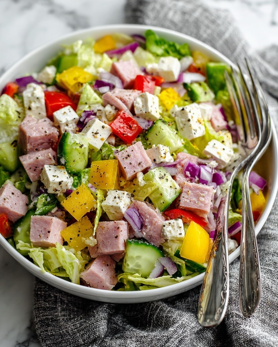 A white bowl filled with a colorful chopped salad sits on a textured grey cloth over a white marbled surface. The salad has many layers showing small square and triangular pieces: bright green lettuce as the base, mixed with light pink chunks of turkey or ham, creamy white cheese cubes, purple onion pieces, red bell peppers, light green cucumber, and yellow pepper slices. Two silver forks rest inside the bowl on the right side, partly buried in the salad. The salad looks fresh and mixed with small black pepper flakes visible. photo taken with an iphone --ar 4:5 --v 7