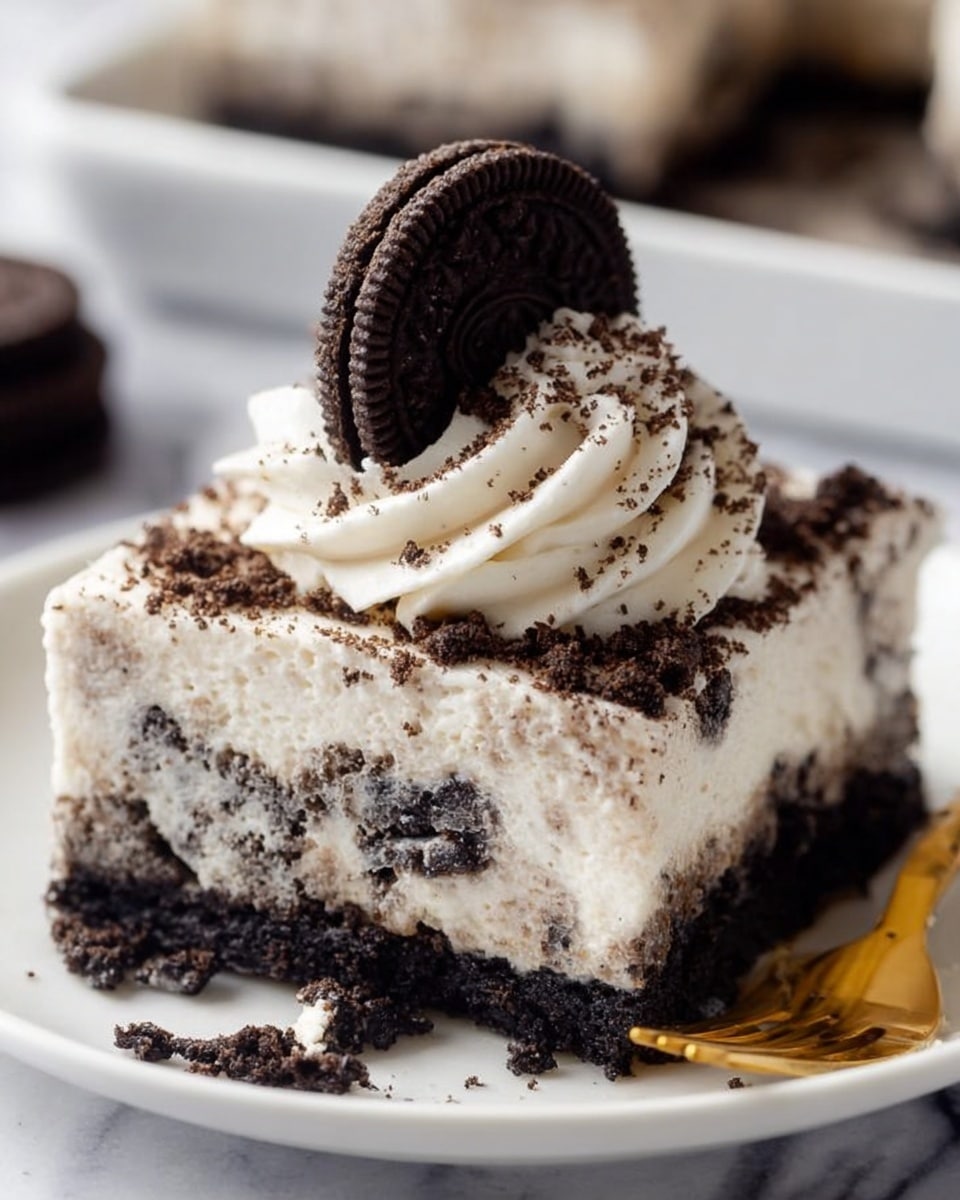 A square slice of Oreo dessert sits on a white plate with a white marbled background, showing two main layers: a dark, crumbly cookie base and a thick, creamy white layer mixed with small cookie pieces. On top is a swirl of whipped cream sprinkled with fine cookie crumbs, crowned by a whole Oreo cookie standing upright. The textures range from smooth cream to crunchy cookie bits, with part of the dessert slightly eaten at the side, showing the creamy inside. A golden fork rests nearby, slightly touching the plate. Photo taken with an iphone --ar 4:5 --v 7