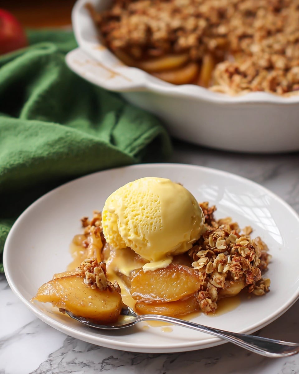 The image shows a white plate with a slice of baked apple crisp topped with a scoop of yellow vanilla ice cream. The dessert has two layers: the bottom layer is soft, golden cooked apple slices with a syrupy texture, and the top layer is a crunchy, golden brown oat crumble with visible oats and small nut pieces. A silver spoon rests on the plate beside the dessert, holding a piece of the apple crisp dripping with syrup. In the background, there is a white pot with baked apple crisps inside, placed on a white marbled surface with a green cloth partially visible. Photo taken with an iphone --ar 4:5 --v 7