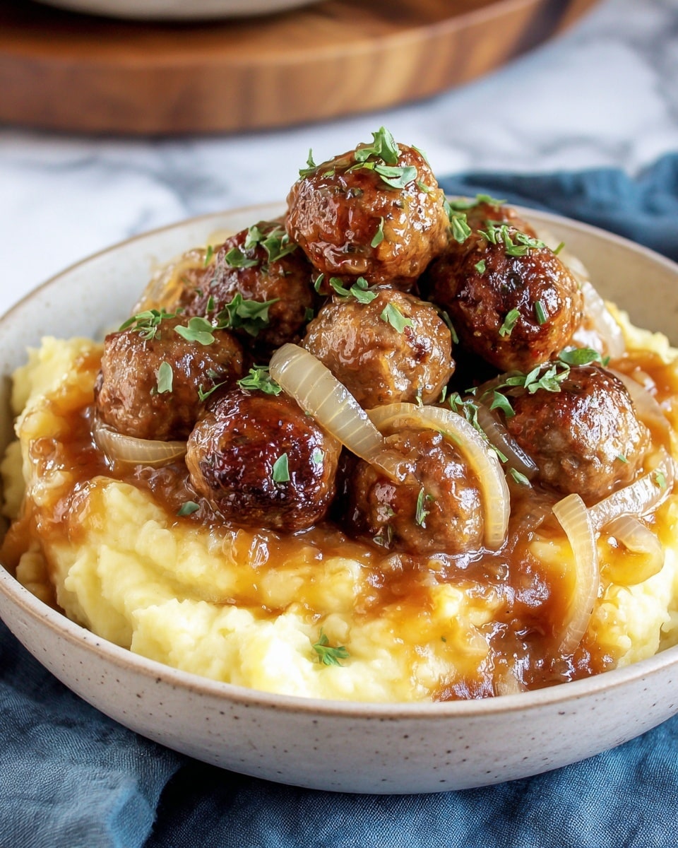 A bowl with a base layer of creamy, pale yellow mashed potatoes with soft texture, topped with a rich brown onion gravy that includes translucent cooked onion slices. On top of this is a pile of shiny, browned meatballs with a slightly crisp exterior, garnished with small green herb pieces scattered over the meatballs. The bowl sits on a blue cloth on a white marbled surface. Photo taken with an iphone --ar 4:5 --v 7