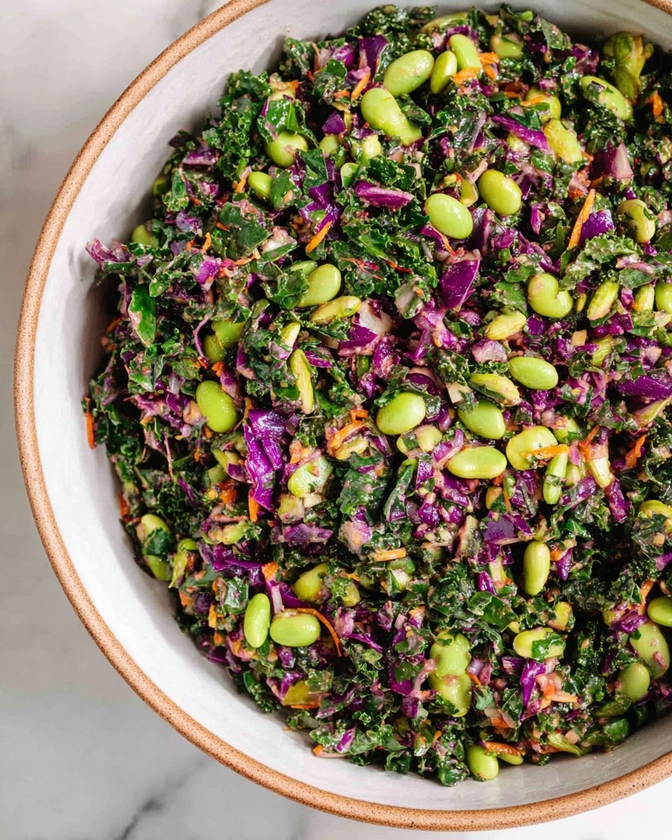 A close-up view of a mixed salad in a white bowl with a light brown rim, showing a colorful mix of finely chopped dark green kale, bright green edamame beans, and small pieces of purple cabbage, along with bits of orange carrot and fresh herbs scattered throughout. The ingredients create a textured, vibrant pattern with contrasting green, purple, and orange colors evenly mixed, resting on a white marbled surface. photo taken with an iphone --ar 4:5 --v 7