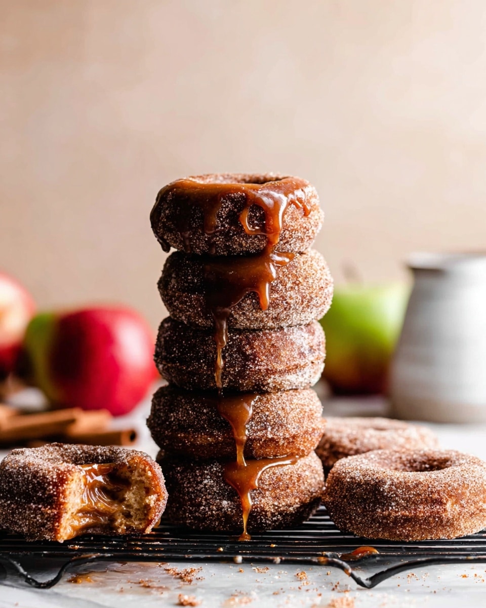 A stack of five dark brown cinnamon sugar donuts with a grainy texture sits on a black cooling rack over a white marbled surface, each donut thick and coated in cinnamon sugar with sticky caramel sauce drizzling down the sides. Next to the stack, two more sugar-coated donuts lay on the surface, one with a bite taken out showing a soft inside. Two apples, one red and one green, are blurred in the background along with a white jar. The scene is warm and inviting with soft natural light. photo taken with an iphone --ar 4:5 --v 7