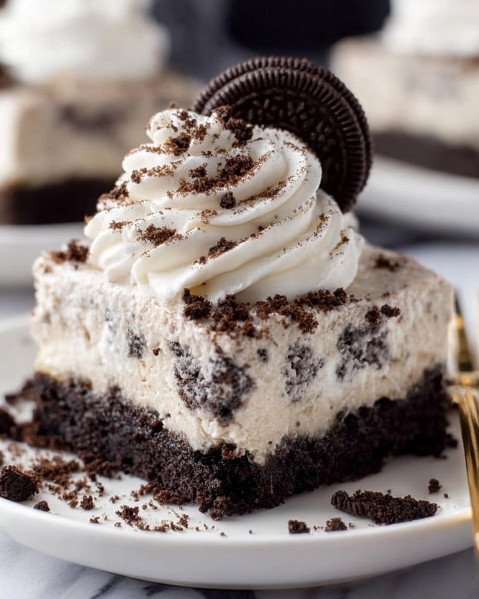 A close-up view of a dessert square on a white plate with a white marbled background. The dessert has two layers: a thick, dark chocolate crumb base that looks firm and dense, and a thick, creamy cookie and cream filling with visible specks of crushed dark cookies mixed throughout. On top of the square, there is a swirl of white whipped cream dusted with fine cookie crumbs, and a whole dark chocolate sandwich cookie standing upright in the center. Some crumbs are scattered around the plate, and a bite is missing from the dessert with a white plate next to it. photo taken with an iphone --ar 4:5 --v 7