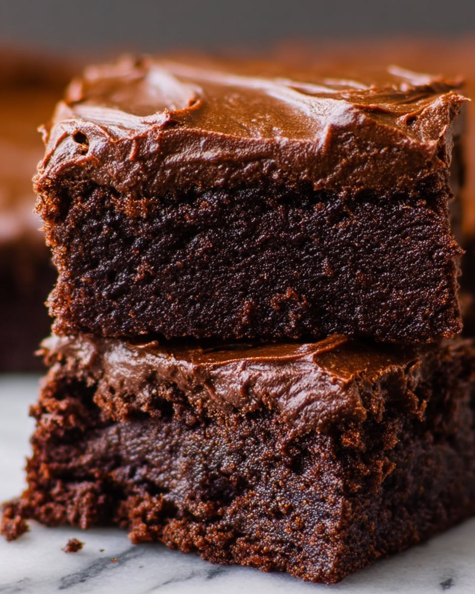 The image shows two thick layers of rich, dark chocolate brownies stacked on each other. The bottom layer has a moist and slightly crumbly texture with a glossy, smooth chocolate frosting spread on top. The top layer has a dense and fudgy inside with the same glossy chocolate frosting that looks creamy and slightly rippled on the surface. The brownies show detailed small cracks on the top frosting layer, adding a homemade feel. The background is a white marbled texture. Photo taken with an iphone --ar 4:5 --v 7