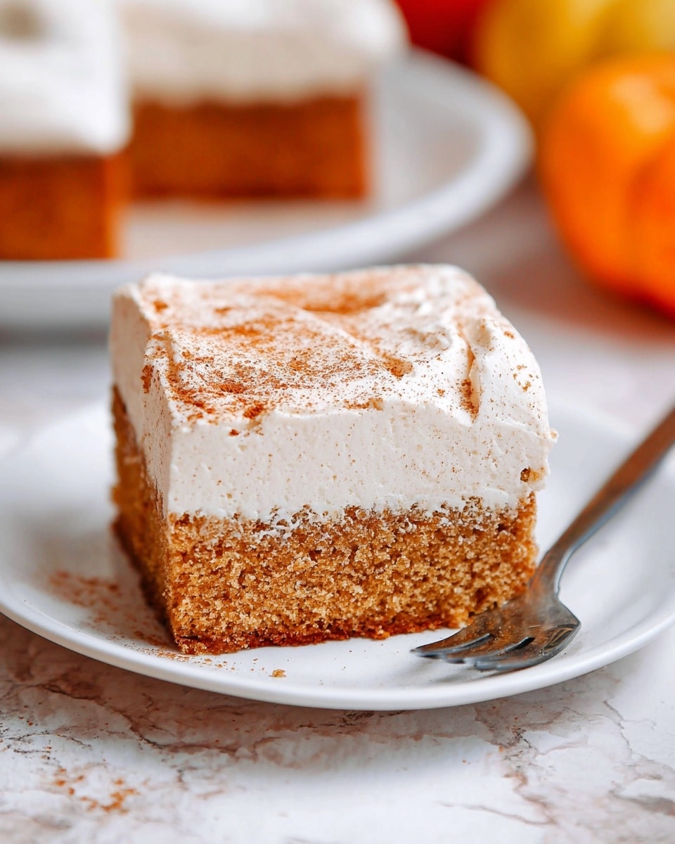 A square piece of cake sits on a white plate, showing two main layers: the bottom layer is a moist, light brown sponge cake with a slightly textured surface, and the top layer is thick, smooth, white frosting dusted with light brown cinnamon powder. The cake is centered with a cinnamon stick and autumn leaves nearby on a white marbled surface. In the background, there are blurred pumpkins and another similar cake piece on a white plate. Photo taken with an iphone --ar 4:5 --v 7