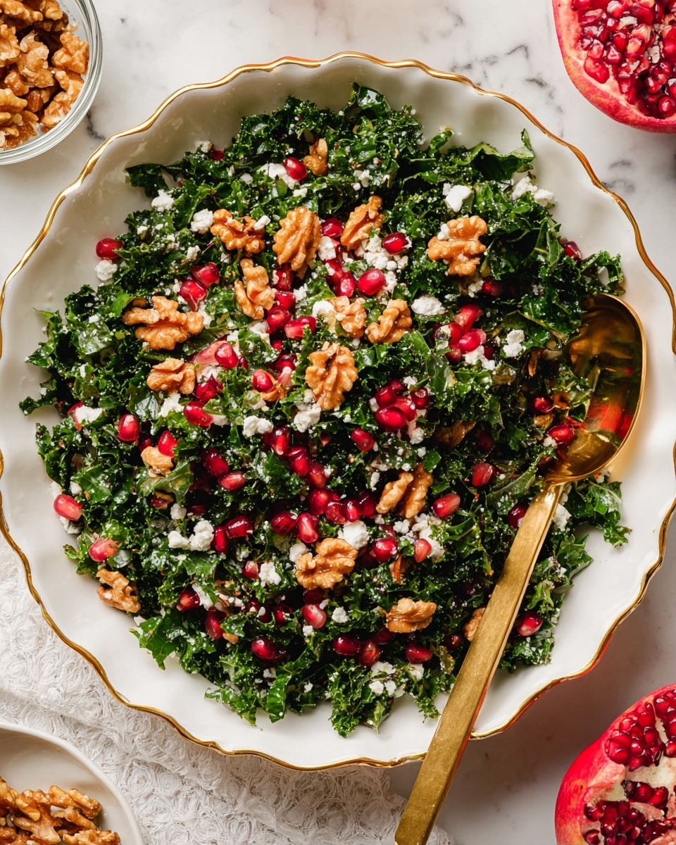A white scalloped bowl with gold trim is filled with a fresh salad made of dark green kale pieces mixed with bright red pomegranate seeds scattered evenly throughout. Light brown walnut halves are placed on top, along with small white cheese crumbles spread across the salad, creating texture and color contrast. A gold spoon rests inside the bowl on the right side, partially buried in the salad. In the background on a white marbled surface, a glass jar and a small white bowl of walnuts are partially visible, along with a halved pomegranate with bright red seeds on the upper right side. Photo taken with an iphone --ar 4:5 --v 7