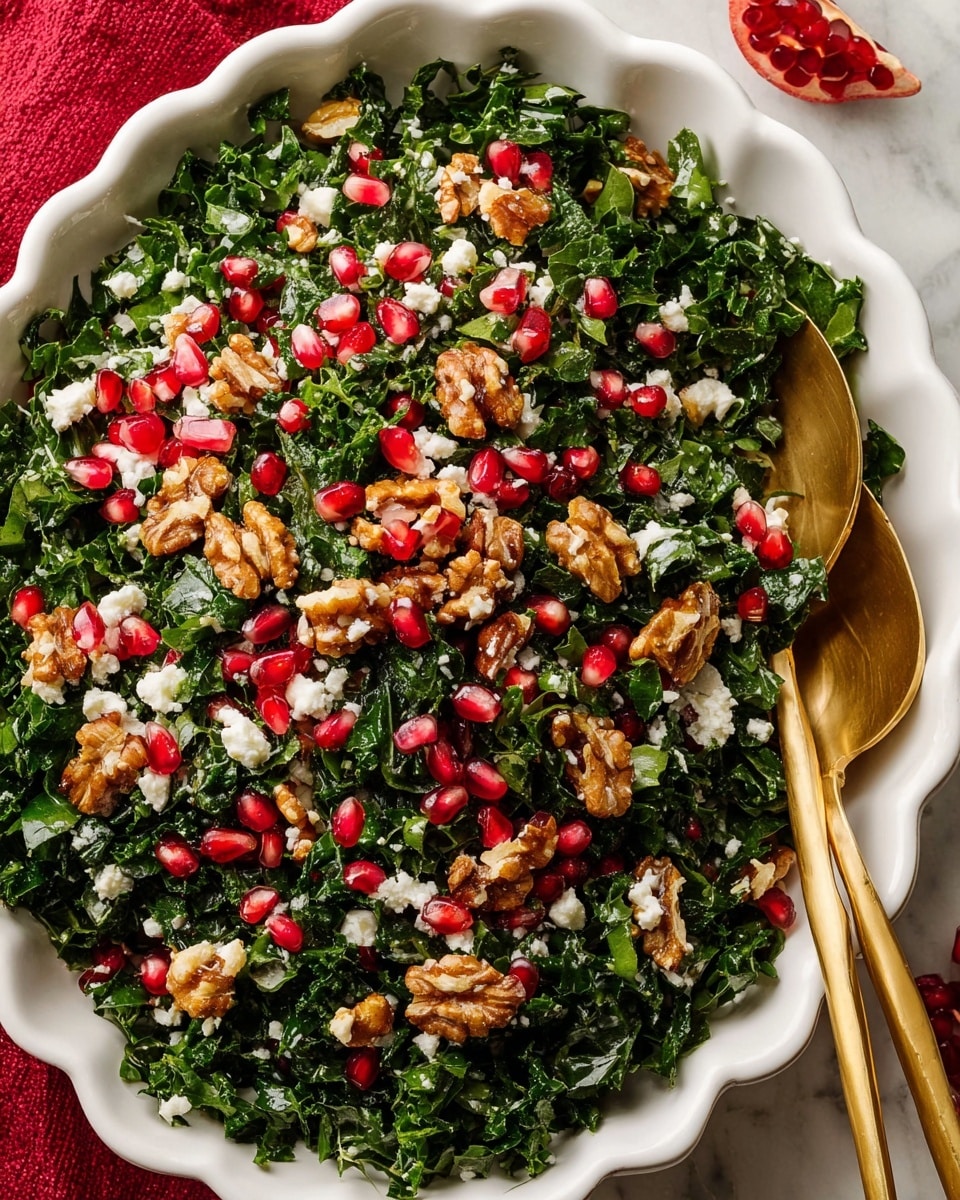 A white scalloped dish filled with a fresh kale salad showing finely chopped dark green kale leaves as the base layer, scattered with bright red pomegranate seeds and medium brown walnut halves on top. Small white crumbles of cheese are spread evenly throughout the salad, adding texture contrast. Two golden serving utensils rest on one side of the dish. The dish sits on a white marbled surface with a hint of a red cloth underneath. Photo taken with an iphone --ar 4:5 --v 7