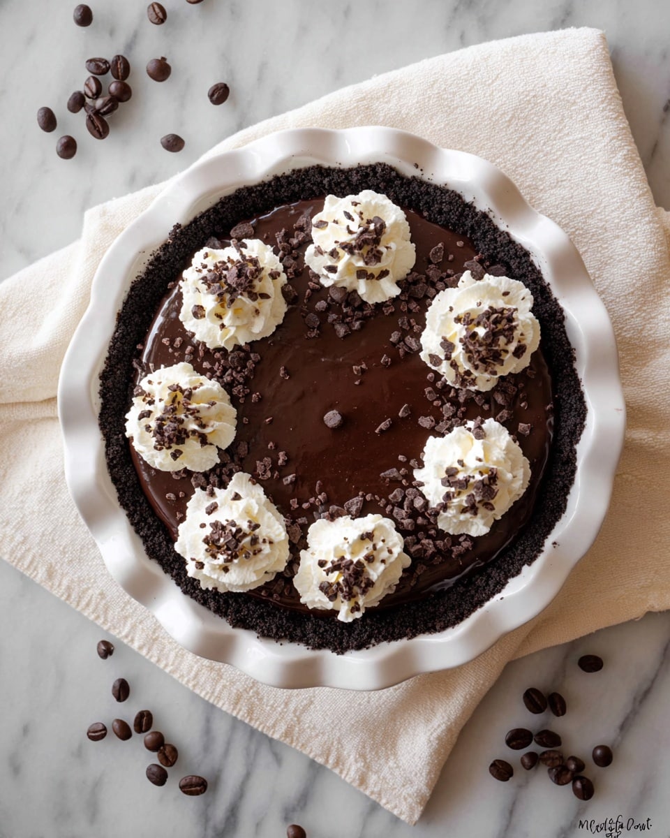 A chocolate pie with three layers is shown on a white fluted pie dish placed on a white marbled surface with a light cloth beneath it. The bottom layer is a dark chocolate cookie crumb crust that lines the dish. The middle layer is a smooth, shiny, thick dark chocolate filling that covers most of the pie's surface. On top, there are eight equal dollops of white whipped cream arranged around the edge, each sprinkled with small chunks of dark chocolate and chocolate crumbs. Around the pie, scattered chocolate-covered coffee beans and coffee beans are placed on the white marbled surface. photo taken with an iphone --ar 4:5 --v 7