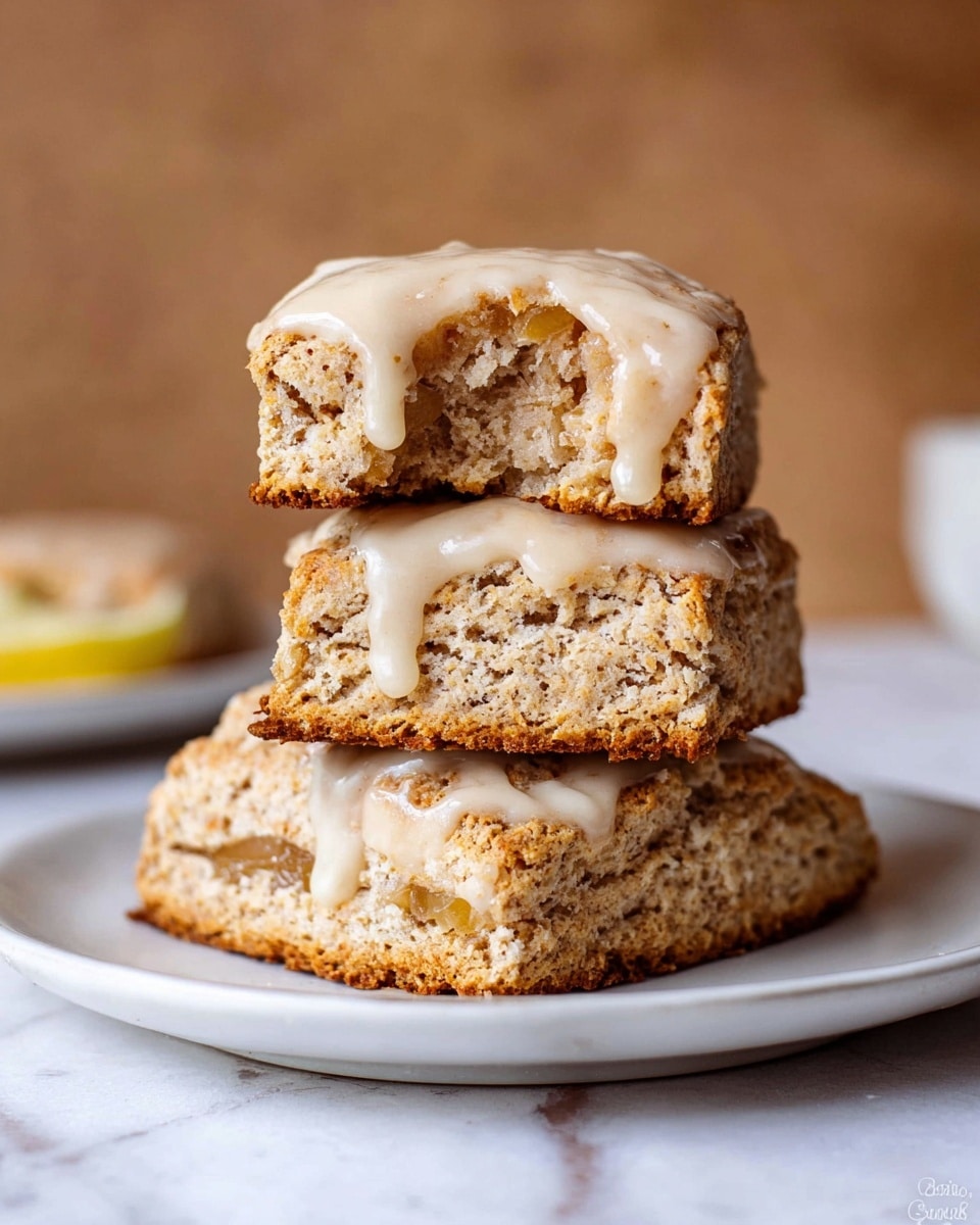 A stack of three square scones sits on a white plate against a soft brown background with a white marbled surface below. The bottom scone is golden brown with visible thin slices of fruit inside its crumb. The middle scone is similar in color and texture with a smooth layer of light beige glaze partly dripping down its sides. The top scone, smaller and shaped more roughly, is topped with an even thicker layer of creamy glaze, showing a crumbly and moist inside with a bite taken out of one side. The overall look is warm and inviting, with a soft, crumbly texture balanced by the smooth glaze. Photo taken with an iphone --ar 4:5 --v 7