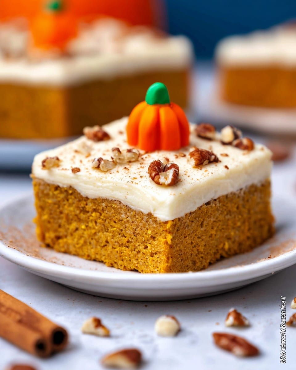 The image shows a single square piece of pumpkin cake placed on a white plate over a white marbled surface. The cake has two layers; the bottom layer is a thick, moist, orange-brown pumpkin cake with a slightly grainy texture. On top is a thinner, smooth layer of creamy white frosting sprinkled with small chopped pecans. A small orange candy shaped like a pumpkin with a green stem sits in the center on top of the frosting. There are some scattered pecans and a light dusting of cinnamon around the cake. The background is softly blurred with warm tones, and a cinnamon stick and another pumpkin candy are visible in the foreground and background. photo taken with an iphone --ar 4:5 --v 7