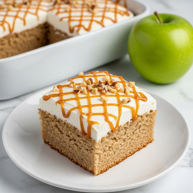 A close-up image shows a square slice of cake on a white plate with ridged edges, placed on a woven mat over a white marbled surface. The cake has two main layers: a thick, light brown moist cake layer at the bottom with a spongy texture, sitting beneath a thick, fluffy white frosting layer. On top of the frosting is a crisscross drizzle of shiny caramel sauce and small pieces of chopped nuts scattered evenly. In the background, there is a green apple and the remaining cake in a metal pan with the same caramel drizzle, all against the white marbled texture. Photo taken with an iphone --ar 4:5 --v 7