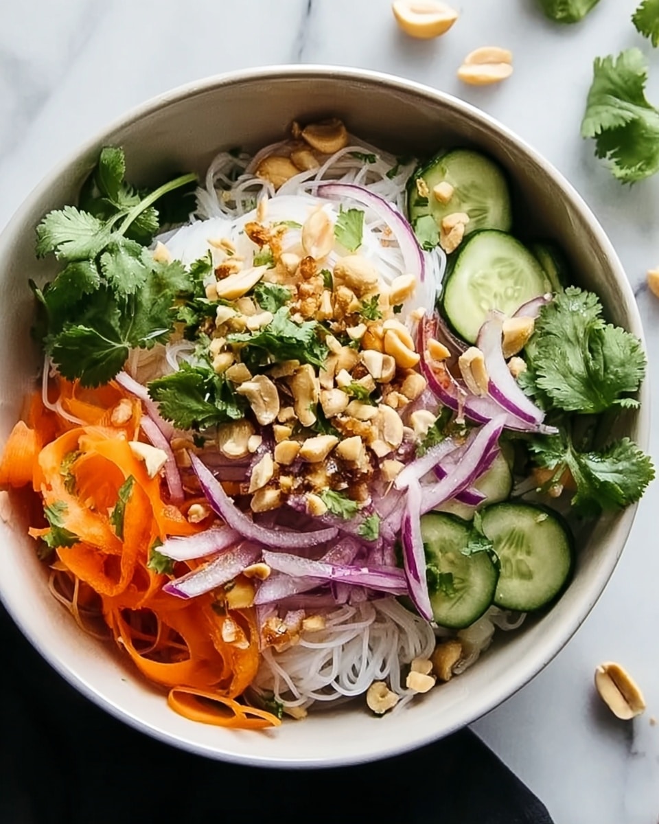 A white bowl filled with several layers of fresh salad ingredients placed on a white marbled surface; the bottom layer consists of thin, white rice noodles, topped with sliced cucumber rounds arranged near the edge, thin orange carrot strips scattered on top, followed by thinly sliced purple onion rings, chopped fresh green cilantro leaves scattered evenly, and a generous sprinkling of roughly chopped light brown peanuts at the center, creating a colorful and textured mix. photo taken with an iphone --ar 4:5 --v 7