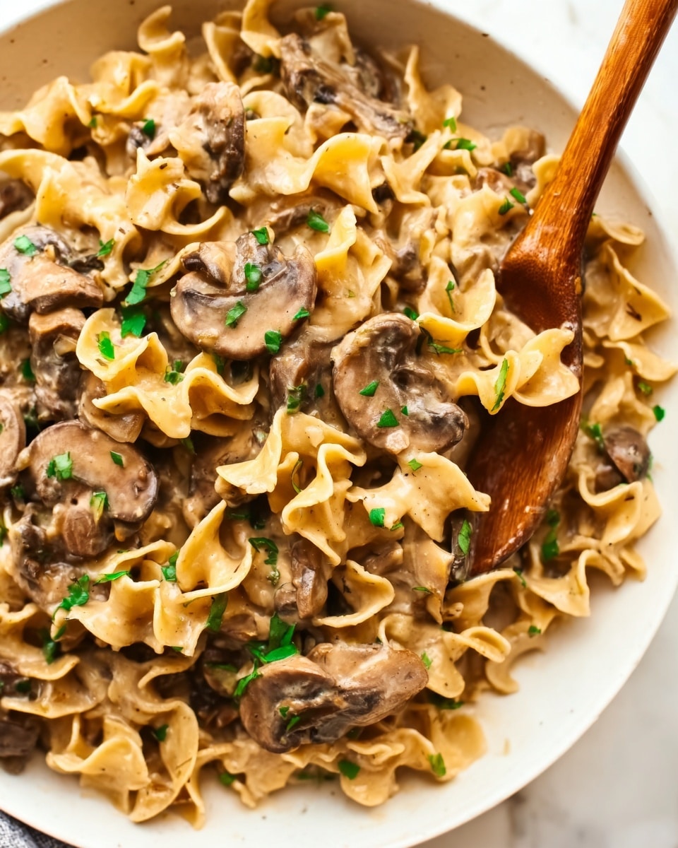 The image shows a white bowl filled with a creamy pasta dish. The pasta is light brown with curly edges, mixed with thin slices of cooked mushrooms that are darker brown. Fresh green herbs are sprinkled on top for color contrast. A wooden spoon is partially inside the bowl, resting on the pasta, with a woman’s hand visible holding the spoon from the side. The bowl sits on a white marbled surface, adding brightness to the presentation. photo taken with an iphone --ar 4:5 --v 7
