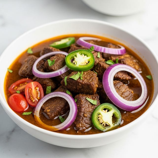 The image shows a bowl filled with a rich stew. The stew has many pieces of browned meat on top, mixed with slices of green jalapeño and bright red tomatoes scattered around. There are soft onion slices that add a different texture and a lighter purplish color to the dish. The bowl is white and placed on a white marbled surface. The stew looks thick and full of spices, with a golden-brown broth covering everything. Photo taken with an iphone --ar 4:5 --v 7