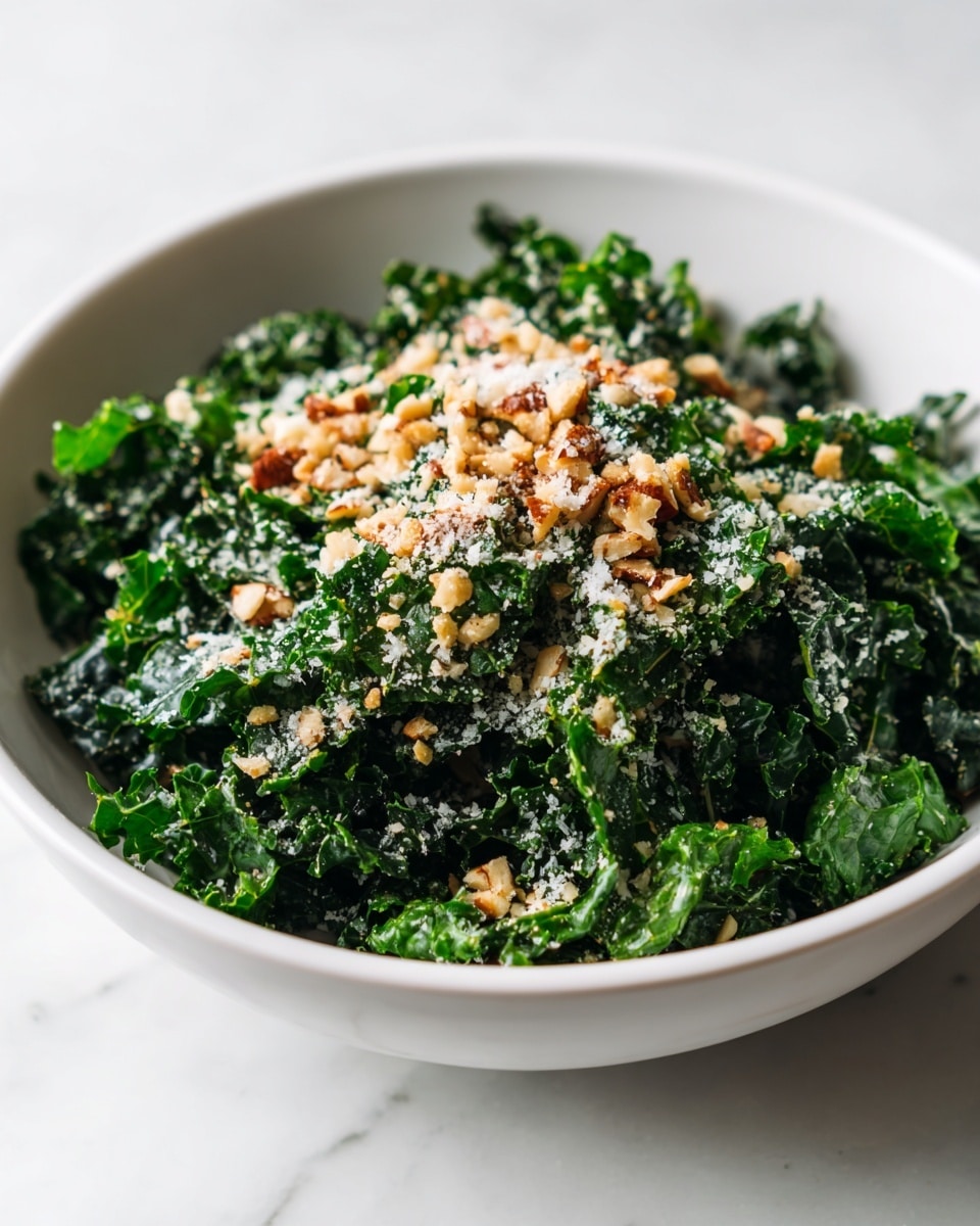 A bowl filled with a fresh kale salad, the dark green leafy kale taking up most of the space, topped with small chunks of light golden breadcrumb-like pieces and finely grated white cheese sprinkled evenly over the surface. The kale leaves are curly and textured, adding a fresh and healthy look, sitting inside a white bowl placed on a white marbled surface. The image is sharp with natural lighting, showing the crispness and detail of each ingredient clearly. Photo taken with an iphone --ar 4:5 --v 7