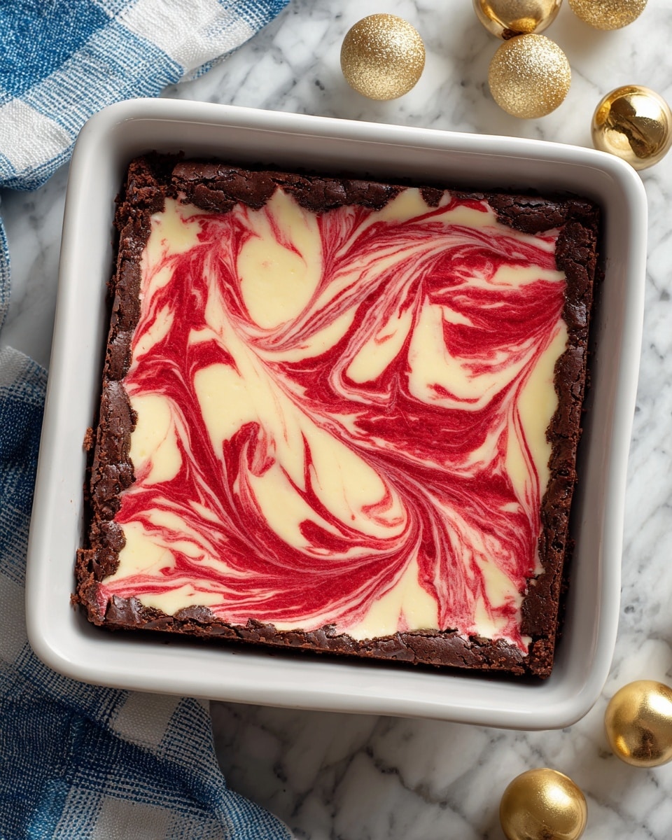 A square dessert sits inside a white square dish, showing two clear layers: the bottom layer is dark chocolate brownie, rough and cracked, forming a thick base and edges around the dish; the top layer is a creamy, smooth cream cheese mixture swirled with bright red, creating a marbled pattern that flows across the surface with rich, velvety red streaks blending into white. The dish is placed on a white marbled texture, with a blue and white checkered cloth partially visible at the top corners and small shiny gold balls nearby. Photo taken with an iphone --ar 4:5 --v 7