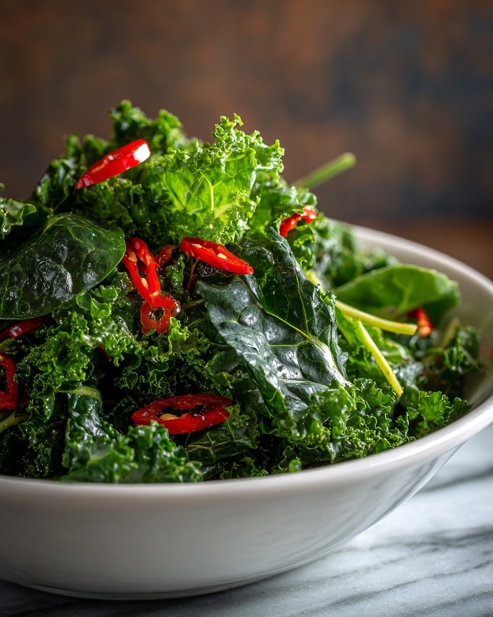 A large metal bowl filled with fresh spinach and kale leaves forms the base layer, their deep green color contrasting with small pieces of bright red chili peppers scattered throughout. The leafy greens are whole and slightly shiny, piled high with some leaves standing upright around the edge of the bowl. The greens have thick, light green stems mixed in, adding texture to the dark leaves. The bowl sits on a dark wooden surface with a worn look, set against a blurred background. photo taken with an iphone --ar 4:5 --v 7