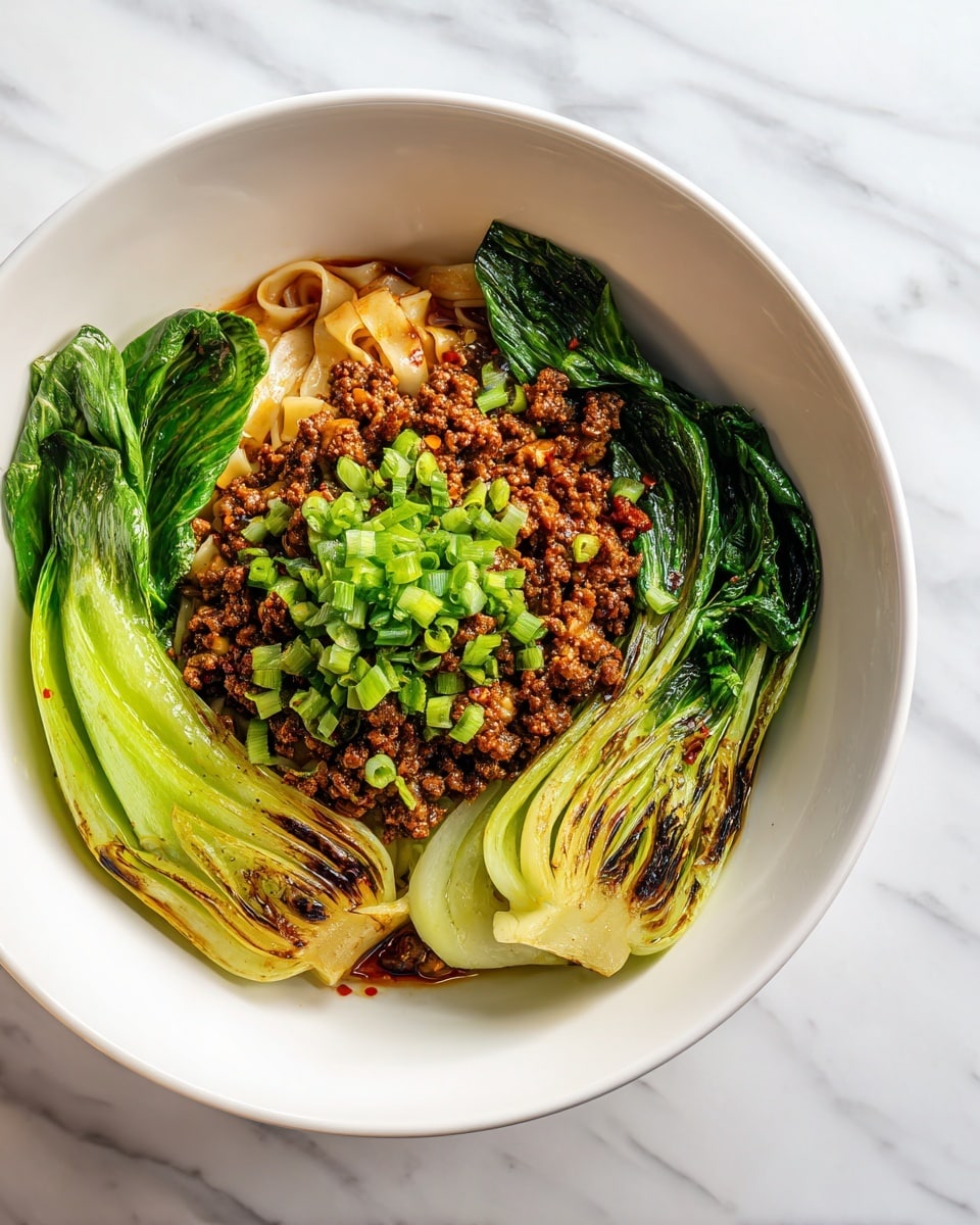 A white bowl filled with three main layers is shown on a white marbled surface. The bottom layer is leafy bok choy with bright and wilted green leaves charred in places and some glossy stem parts. The middle layer is cooked minced meat pieces that are brown with a slightly oily texture scattered over the noodles. The top layer is curly flat noodles coated with a dark reddish-brown spicy sauce, garnished with chopped fresh bright green onions evenly spread over the noodles. The bok choy is positioned around the noodles in the bowl’s edges. photo taken with an iphone --ar 4:5 --v 7