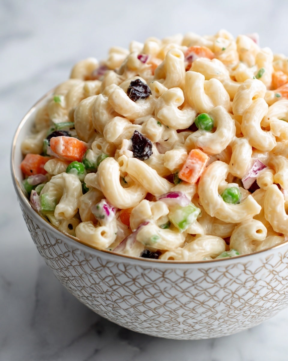 The image shows a close-up of a white patterned bowl filled with creamy pasta salad. The dish has three main layers: the base is curved elbow macaroni pasta colored pale yellow with a smooth texture, mixed throughout with small cubes of orange carrot and green celery for a crunchy look, and scattered dark blue-black raisins for contrast. The pasta and veggies are coated evenly in a thick white creamy dressing that adds a glossy texture over everything. The bowl sits on a wooden surface. photo taken with an iphone --ar 4:5 --v 7